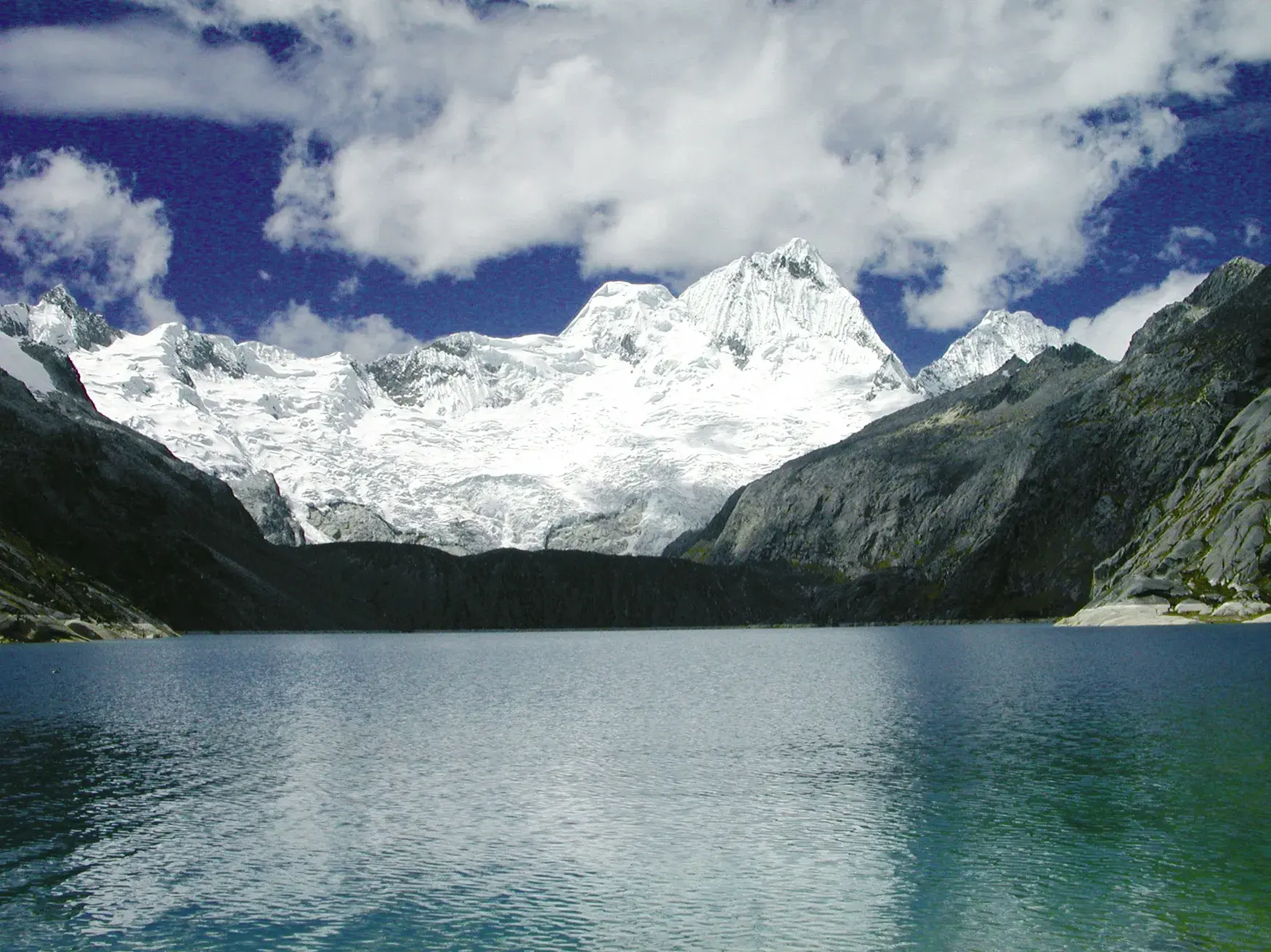 Blick beim Trekking in der Cordillera Blanca über eine Lagune auf den schneebedeckten Gipfel des Berges Taulliraju.