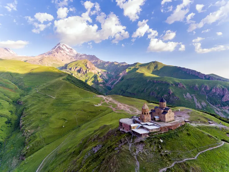 Die Gergetier Dreifaltigkeitskirche thront auf einem grünen Hügel vor dem schneebedeckten Gipfel des Kasbek in Georgien.