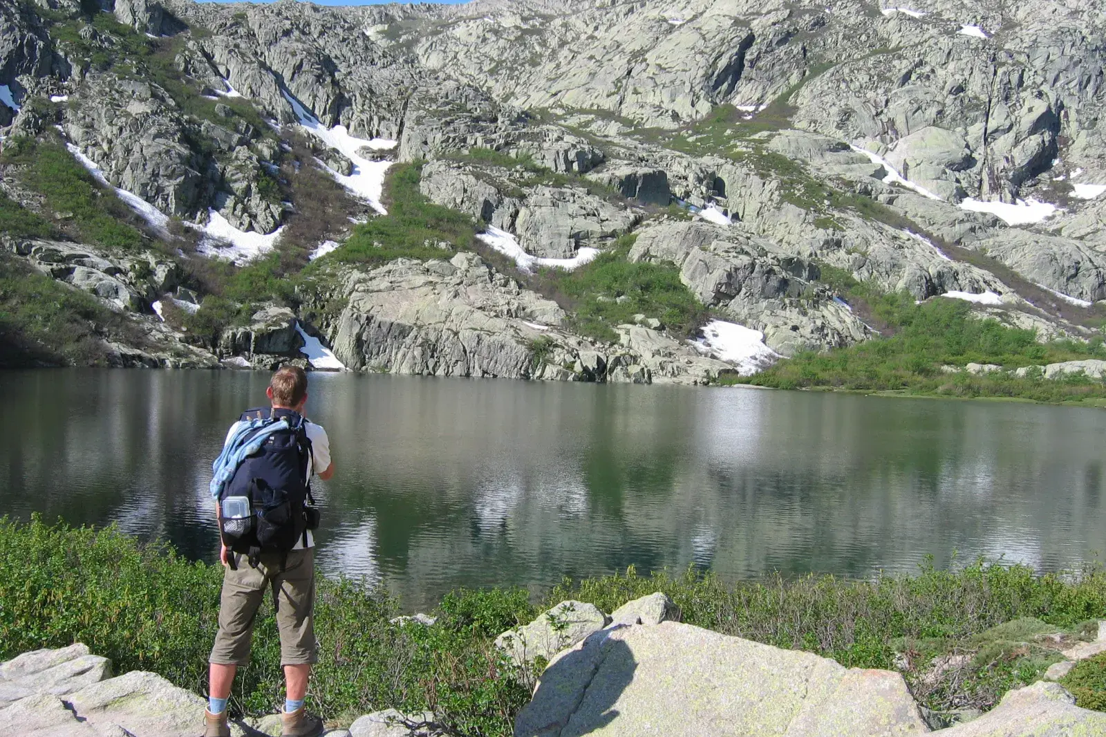 Trekking auf dem GR20: Ein Wanderer macht eine Pause an einem klaren Gletschersee inmitten des korsischen Bergmassivs.