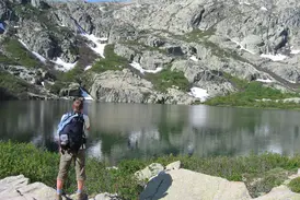 Trekking auf dem GR20: Ein Wanderer macht eine Pause an einem klaren Gletschersee inmitten des korsischen Bergmassivs.