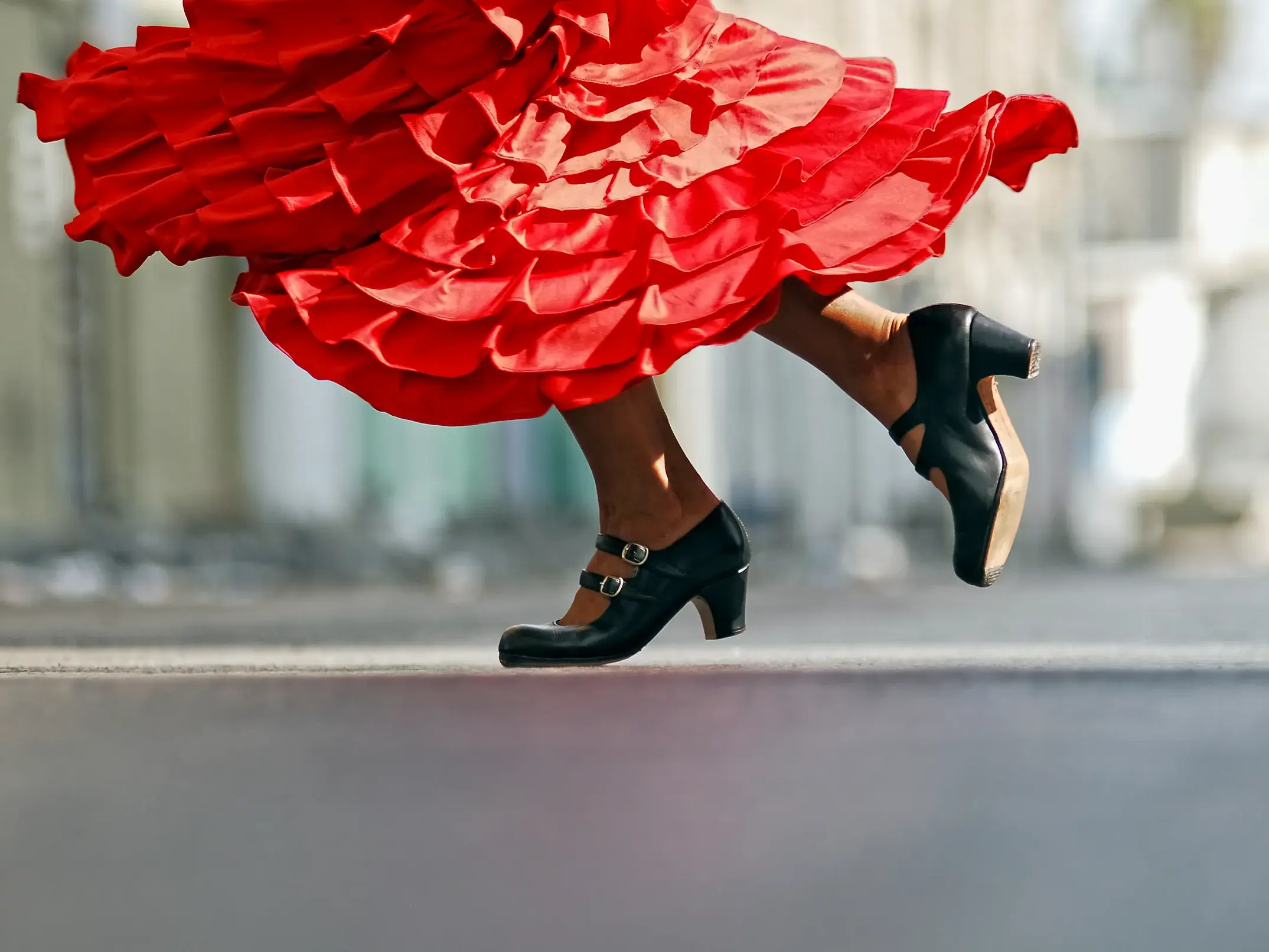 Nahaufnahme der Füße einer Flamenco-Tänzerin in schwarzen Schuhen und einem wirbelnden roten Kleid auf einer Straße in Andalusien.
