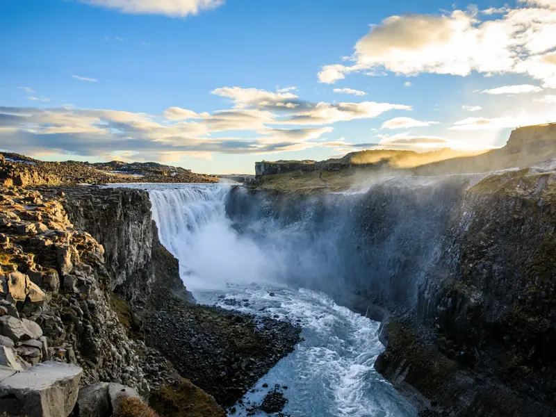 Der mächtige Dettifoss Wasserfall in Island stürzt bei Sonnenuntergang tosend in eine dunkle, felsige Schlucht.
