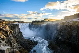 Der mächtige Dettifoss Wasserfall in Island stürzt bei Sonnenuntergang tosend in eine dunkle, felsige Schlucht.