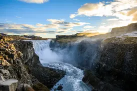Der mächtige Dettifoss Wasserfall in Island stürzt bei Sonnenuntergang tosend in eine dunkle, felsige Schlucht.