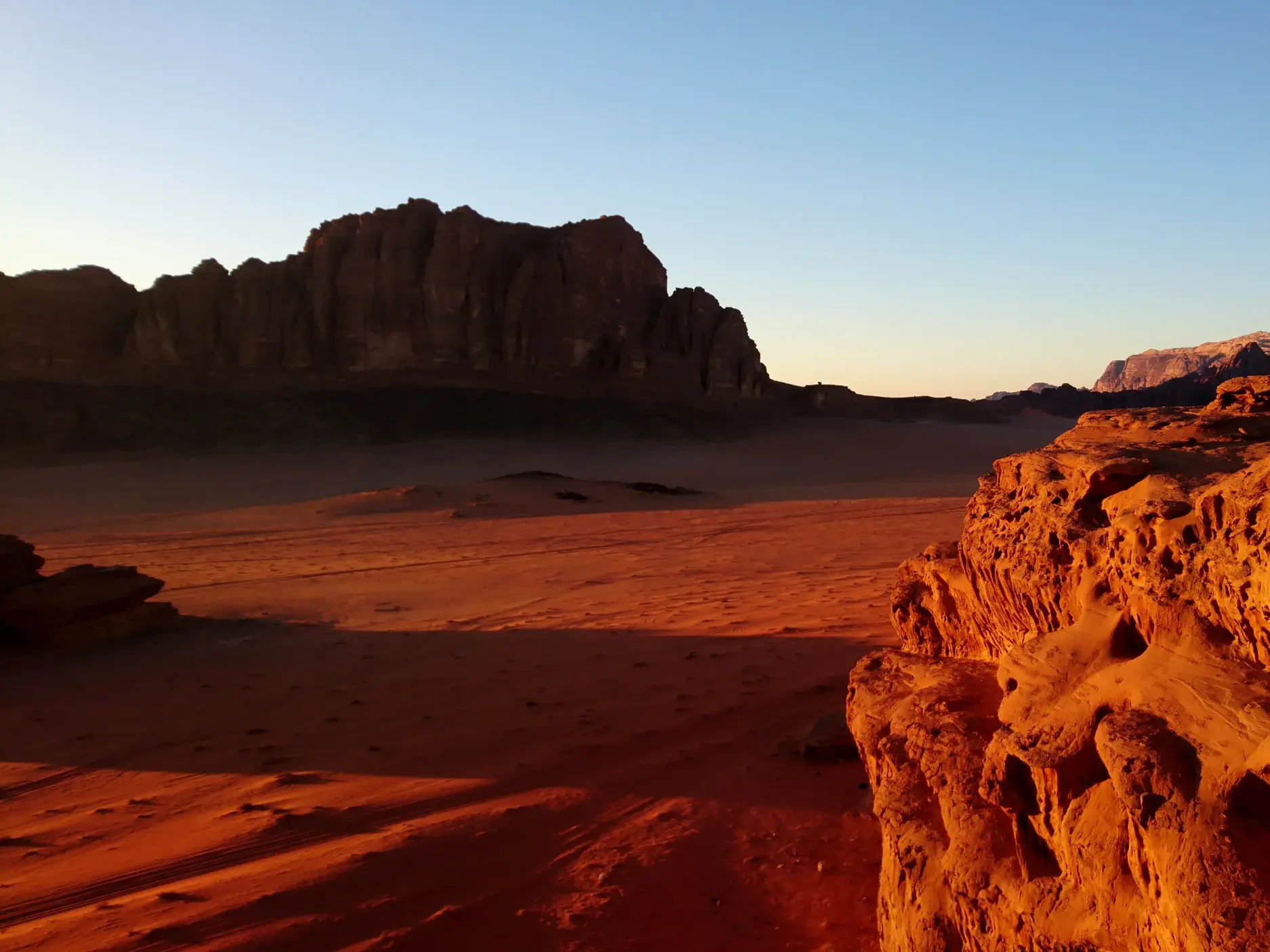 Die Abendsonne taucht die bizarren Sandsteinfelsen und roten Dünen der Wüste Wadi Rum in Jordanien in warmes Licht.