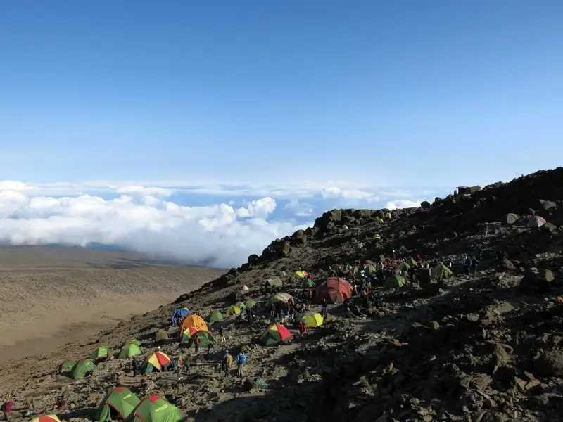 Zahlreiche bunte Trekking-Zelte im Barafu Camp am Kilimandscharo, aufgebaut an einem felsigen Hang hoch über den Wolken.