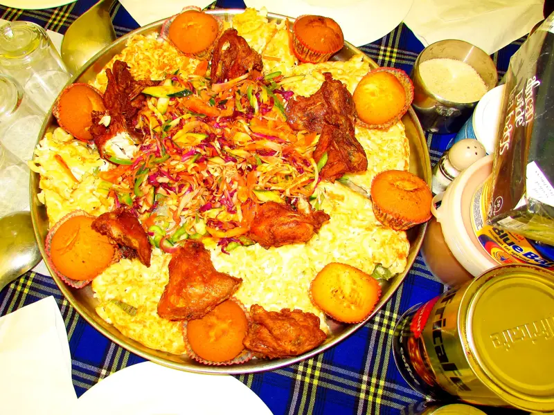 Ein reichhaltiges, landestypisches Festmahl in Tansania mit Hähnchen, Reis und Muffins wird auf einer großen Platte serviert.