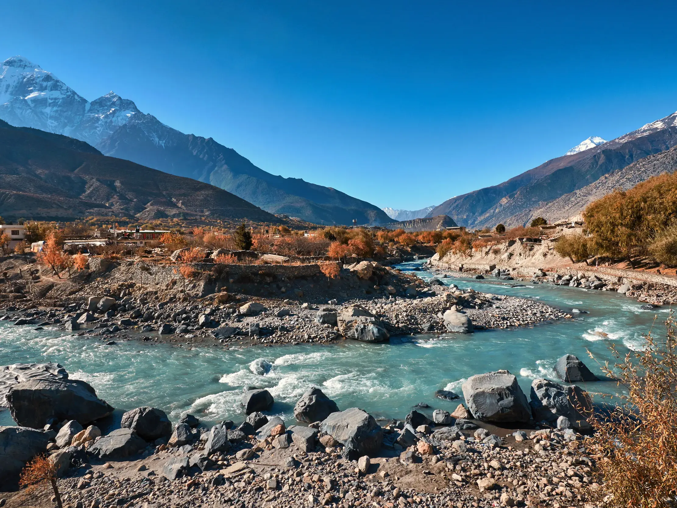 Der türkise Kali Gandaki Fluss im weiten Tal von Mustang, Nepal, mit Blick auf die schneebedeckten Gipfel des Himalaya.