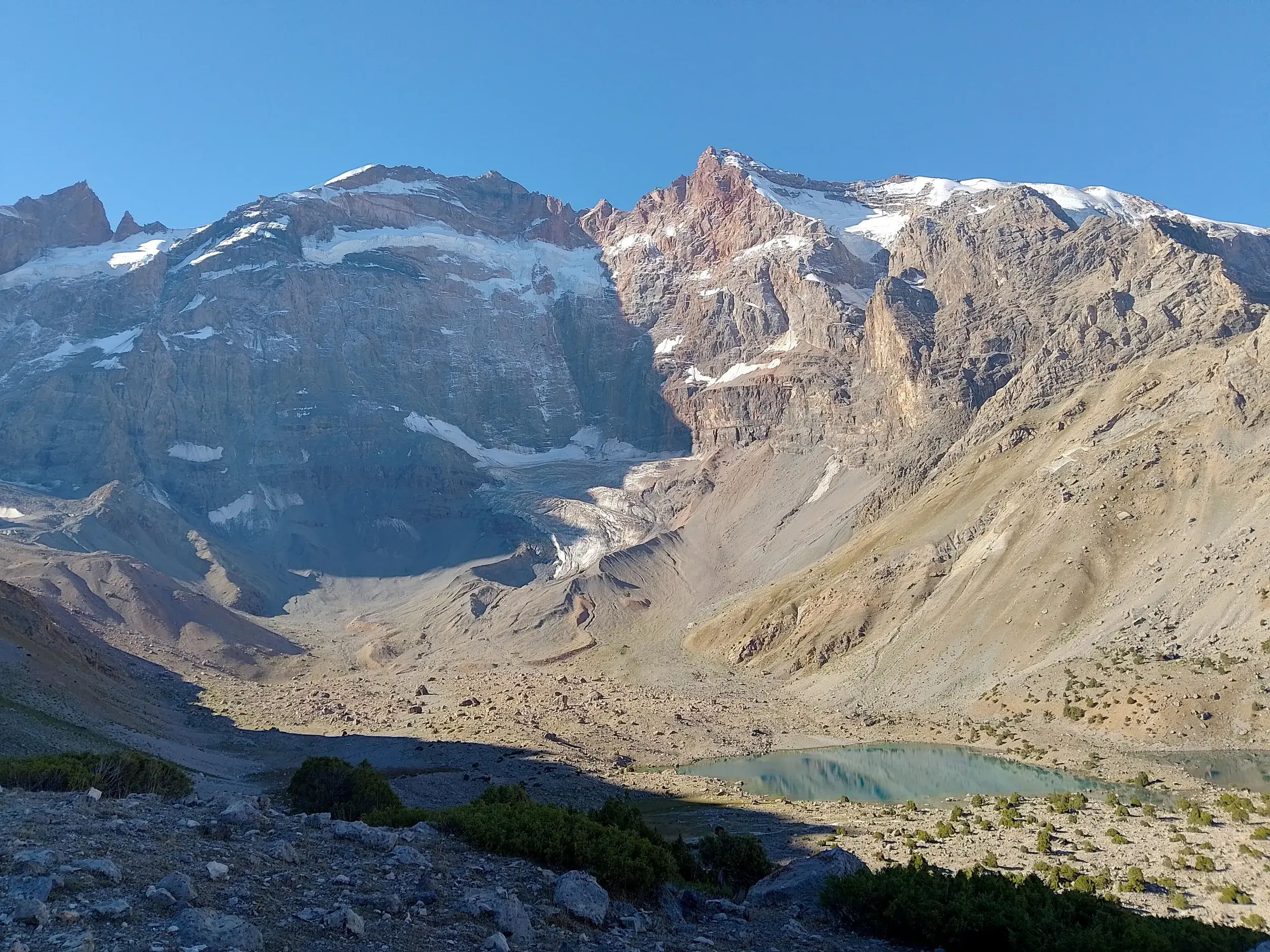 Panoramablick auf den Gletschersee Mutnyi-See, umgeben von schneebedeckten Fünftausendern im Fan-Gebirge in Tadschikistan.