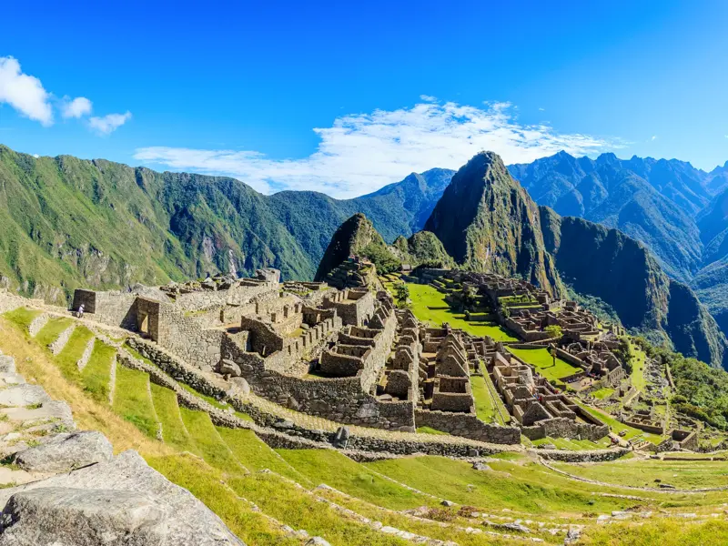 Sonnige Panoramaansicht der weltberühmten Inkastadt Machu Picchu in Peru mit ihren grünen Terrassen und Andengipfeln.