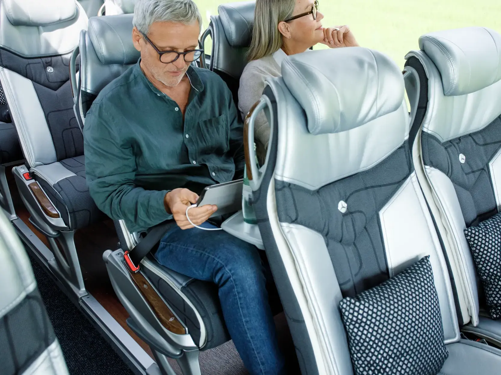 Ein Reisender entspannt sich auf einem bequemen Sitz im modernen Studiosus-Komfortbus und lädt sein Tablet.