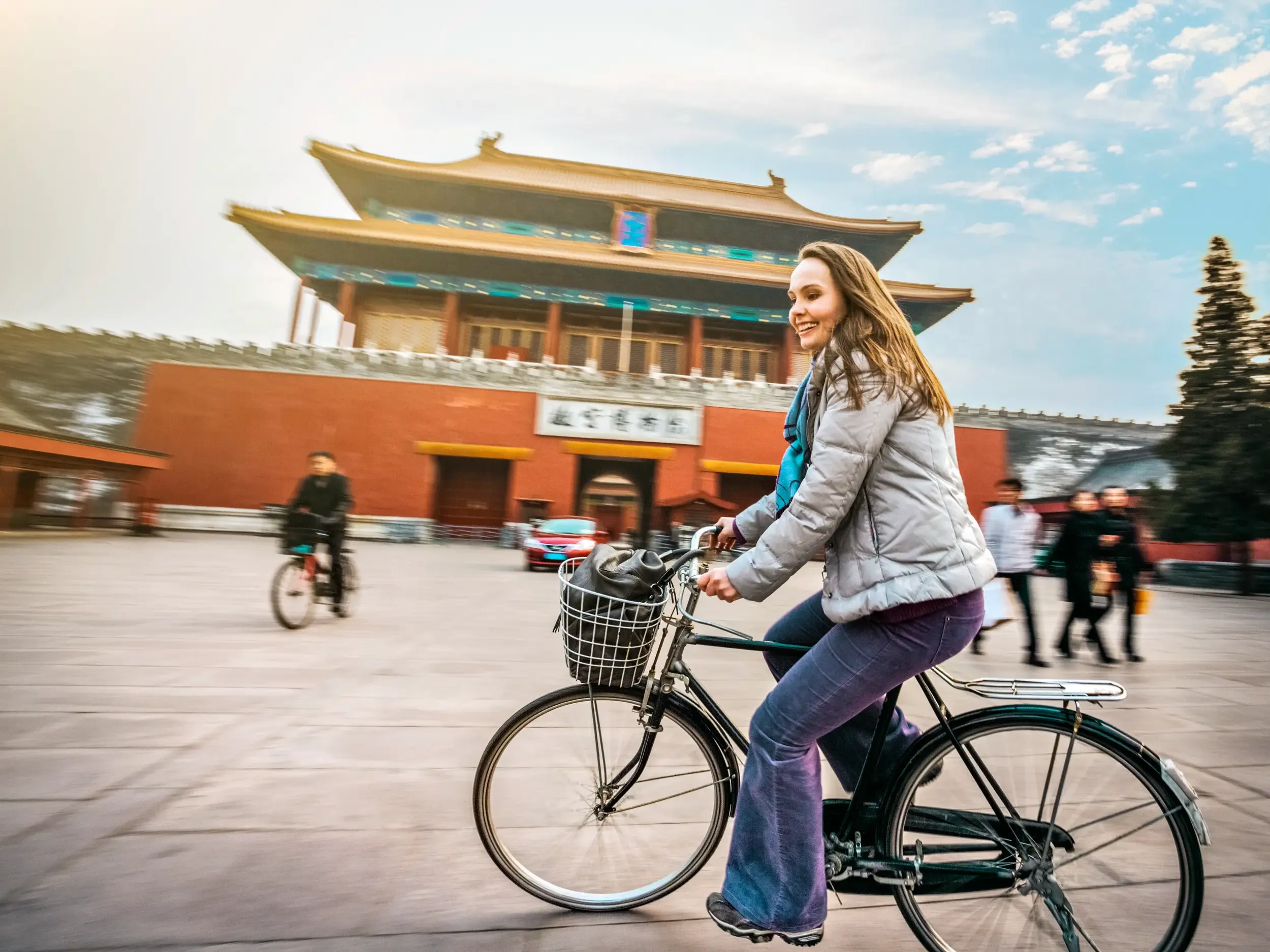 Lächelnde junge Frau radelt über den weiten Platz vor der Verbotenen Stadt in Beijing.