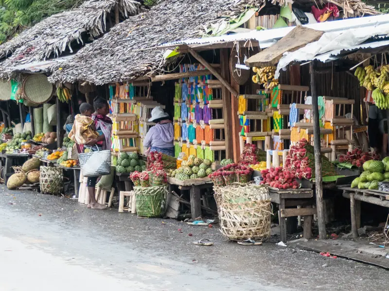 Einheimische Frauen an einem bunten Marktstand am Straßenrand in Madagaskar mit frischen Früchten und lokalem Handwerk.