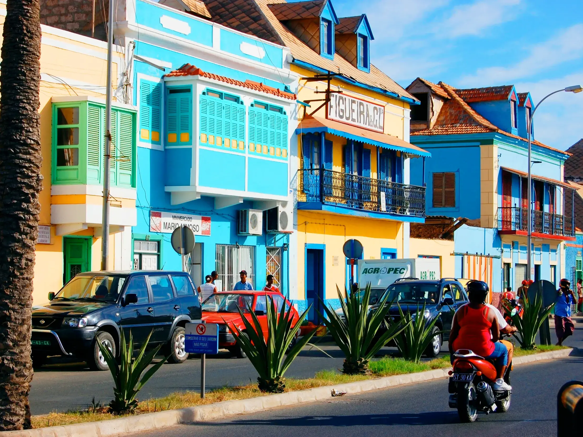 Lebhafte Straßenszene in Mindelo mit farbenfrohen Kolonialhäusern, Palmen und Alltagsverkehr auf der Kapverden-Insel São Vicente.