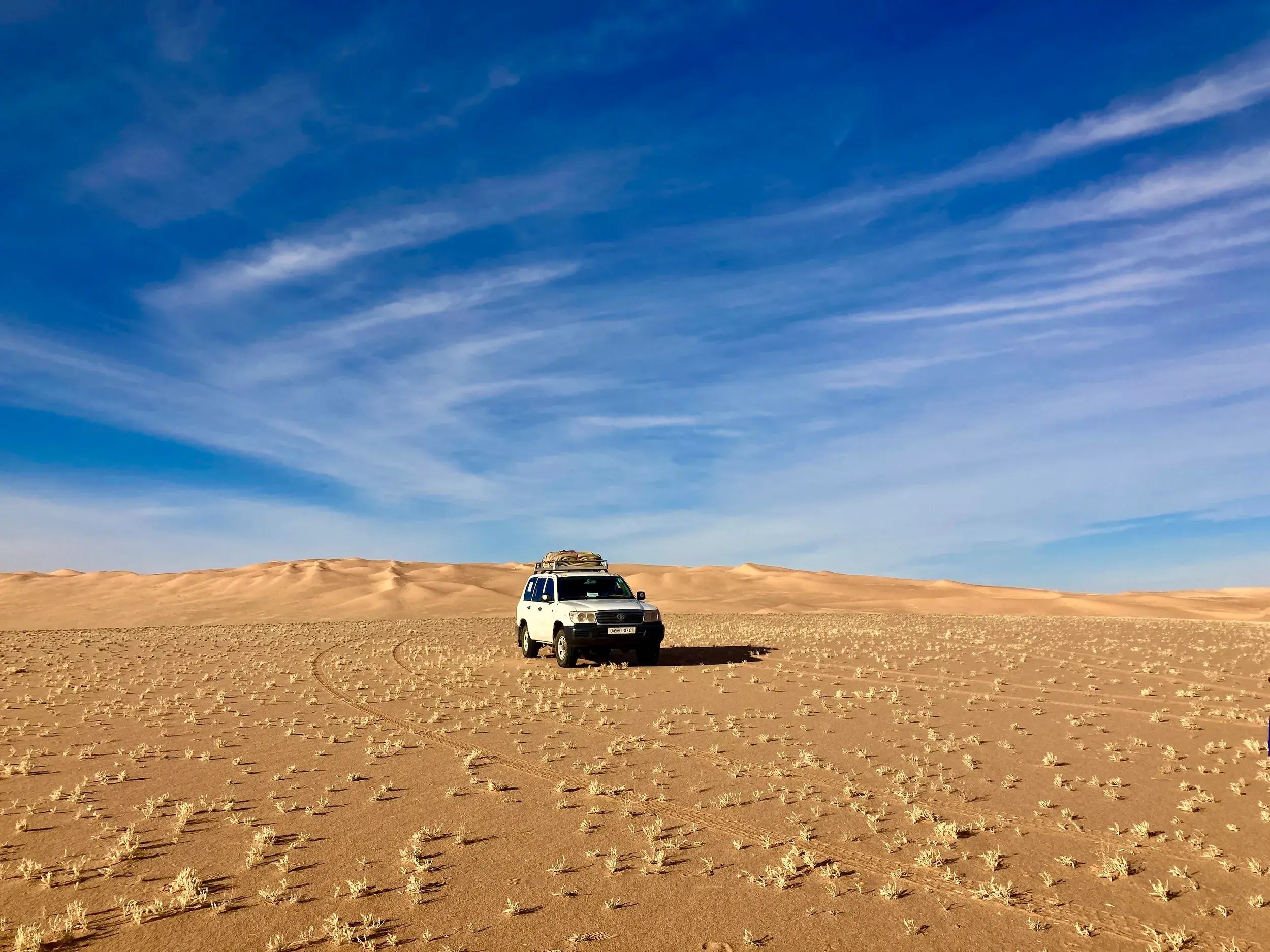 Weißer Geländewagen auf einer Trekking-Expedition vor den Sanddünen des Erg Admer in der algerischen Sahara.