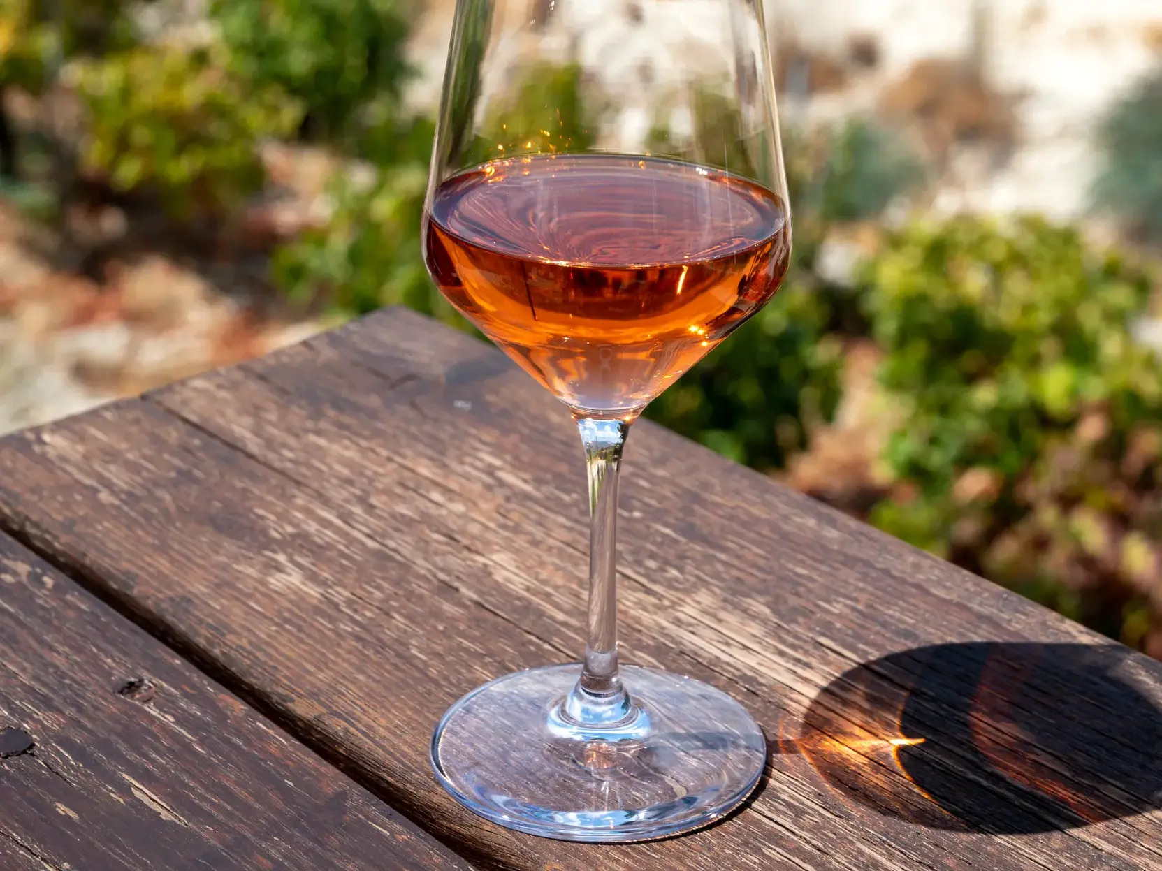 Ein Glas zypriotischer Rosenwein auf einem rustikalen Holztisch, im Hintergrund die sonnige Naturlandschaft Zyperns.