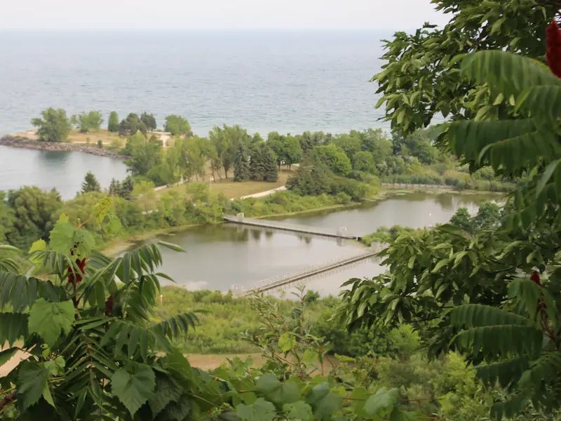 Ausblick von den Scarborough Cliffs in Toronto auf eine grüne Halbinsel und einen Steg am Ufer des weiten Ontario-Sees.