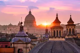 Malerischer Sonnenuntergang über Rom mit Blick auf die Kuppel der Peterskirche und weitere Türme und Kuppeln im Vordergrund.