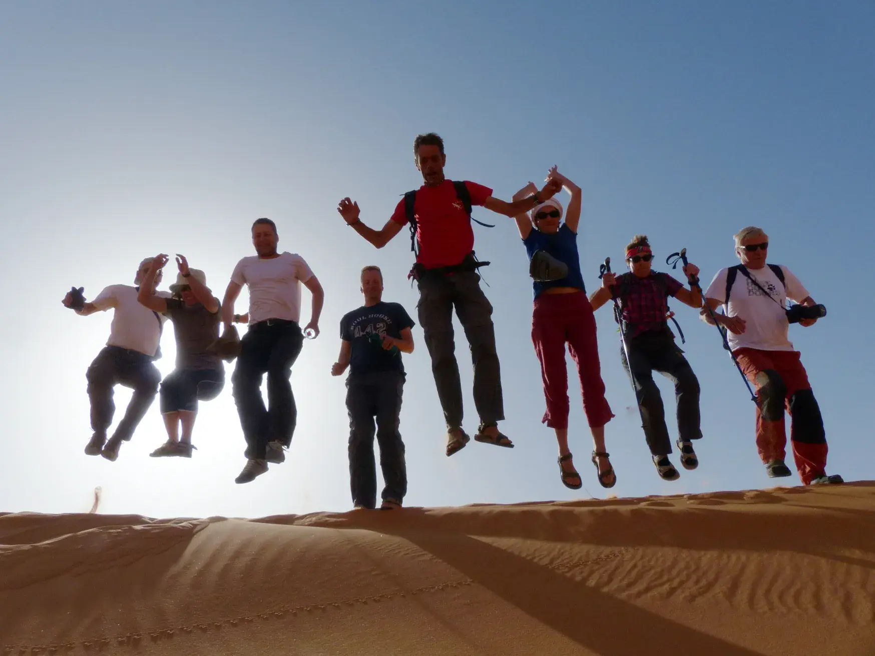 Eine Hauser-Reisegruppe springt beim Wüsten-Trekking ausgelassen von einer Sanddüne in der Erg Chegaga Wüste.
