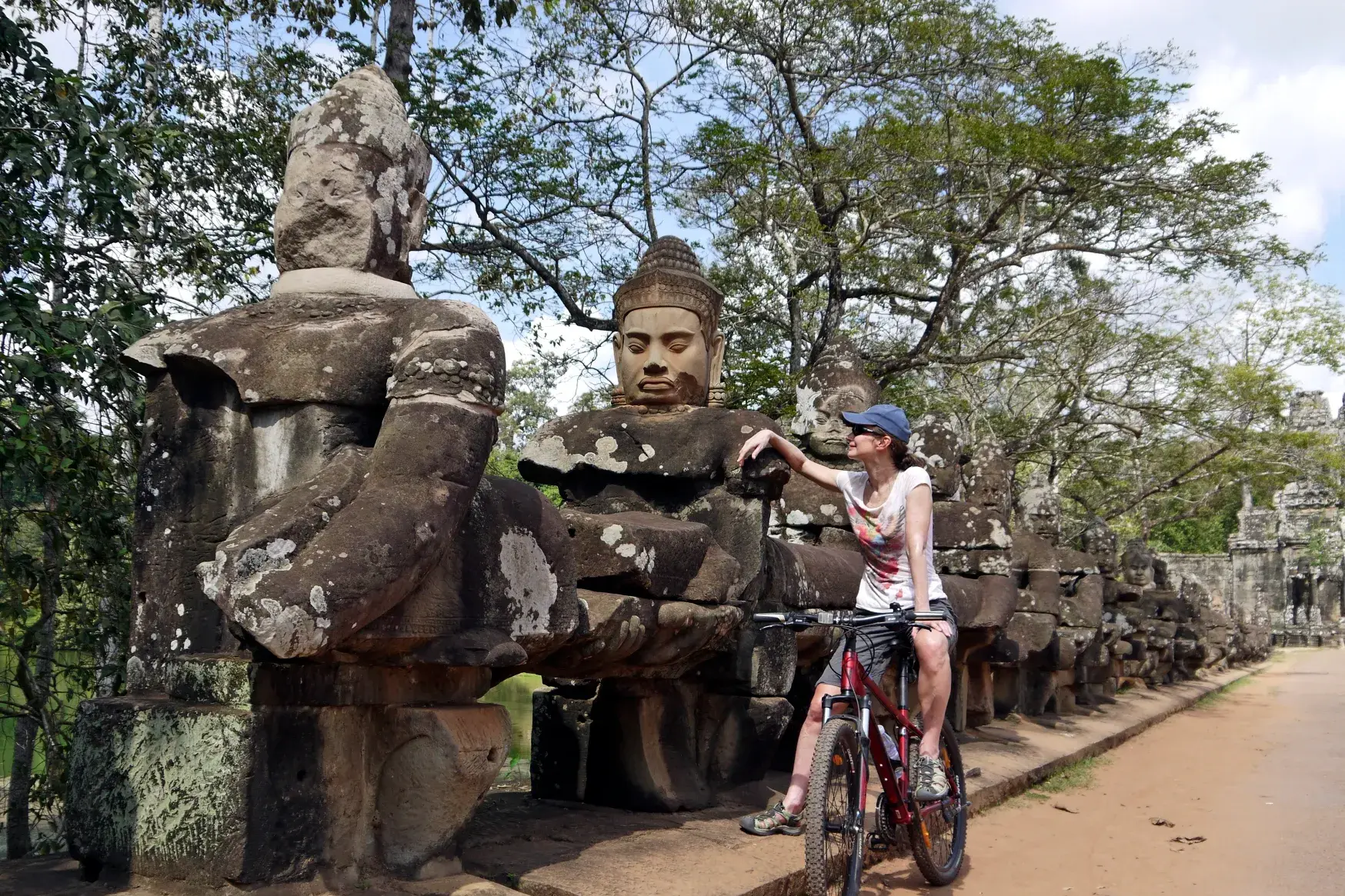 Eine Mountainbikerin macht auf ihrer Radtour eine Pause und bewundert die steinernen Wächterfiguren am Bayon Tempel in Angkor.