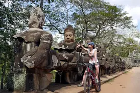 Eine Mountainbikerin macht auf ihrer Radtour eine Pause und bewundert die steinernen Wächterfiguren am Bayon Tempel in Angkor.