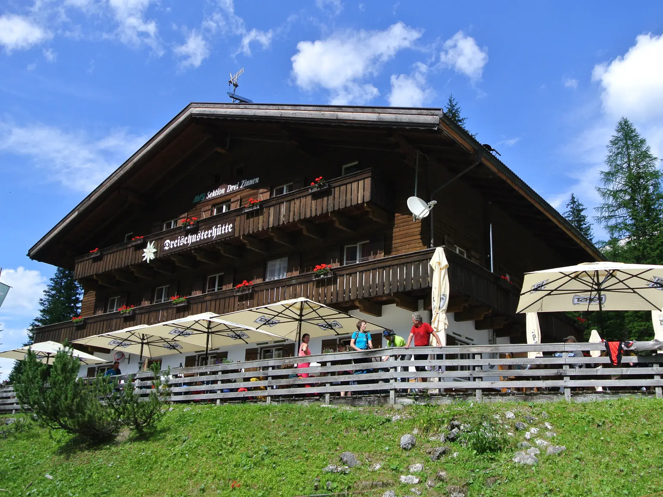 Wanderer genießen die Sonne auf der Terrasse der urigen Dreischusterhütte im Innerfeldtal in den Sextner Dolomiten.