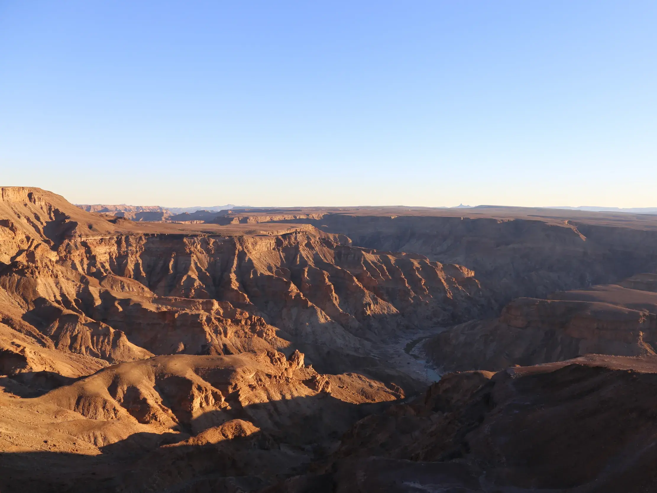 Die tiefstehende Sonne wirft goldenes Licht auf die schroffen Felswände des weiten Fish River Canyon in Namibia.