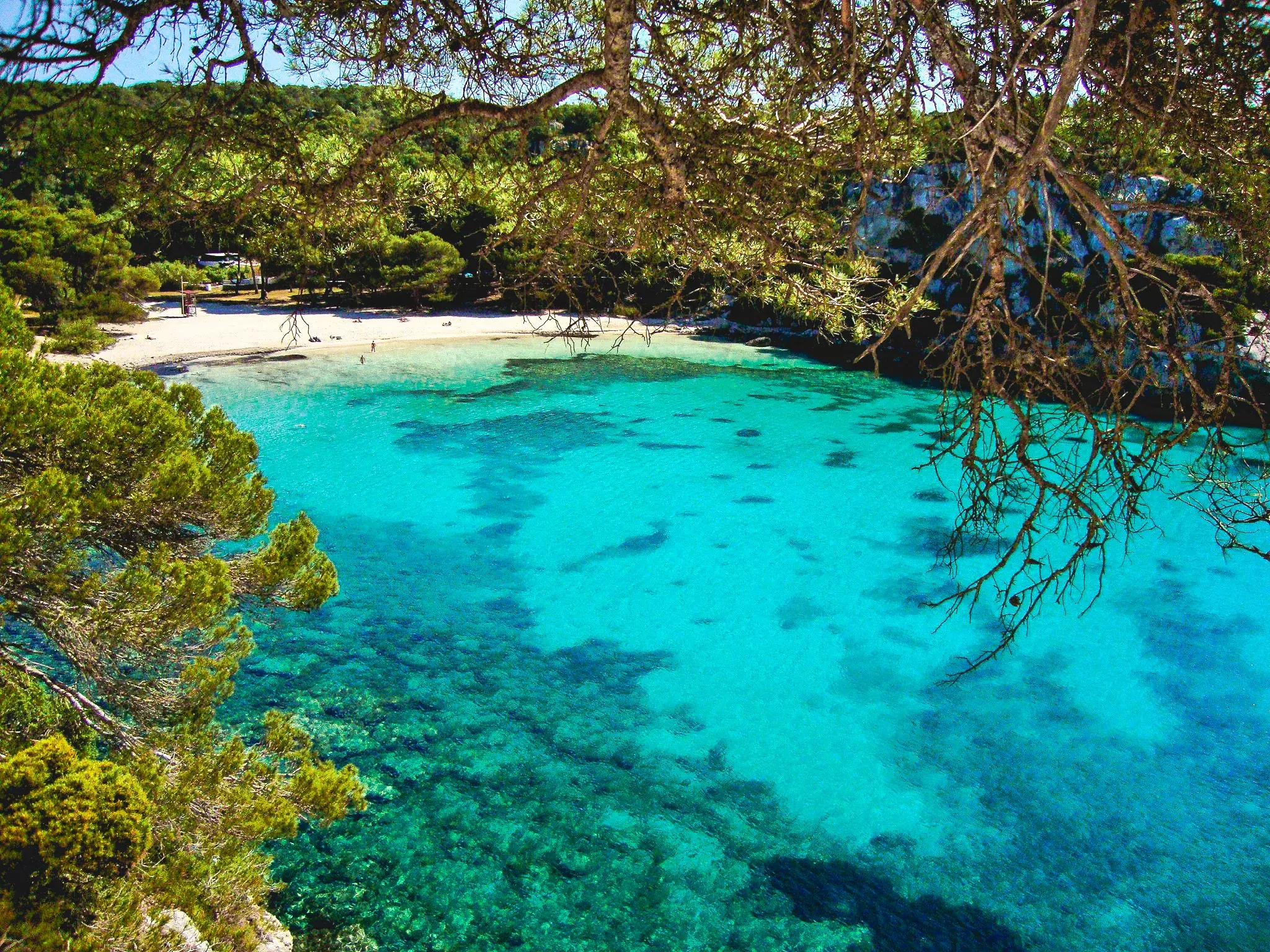 Erhöhter Blick vom Küstenwanderweg auf die Bucht Cala Macarella auf Menorca mit türkisfarbenem Meer und Sandstrand.