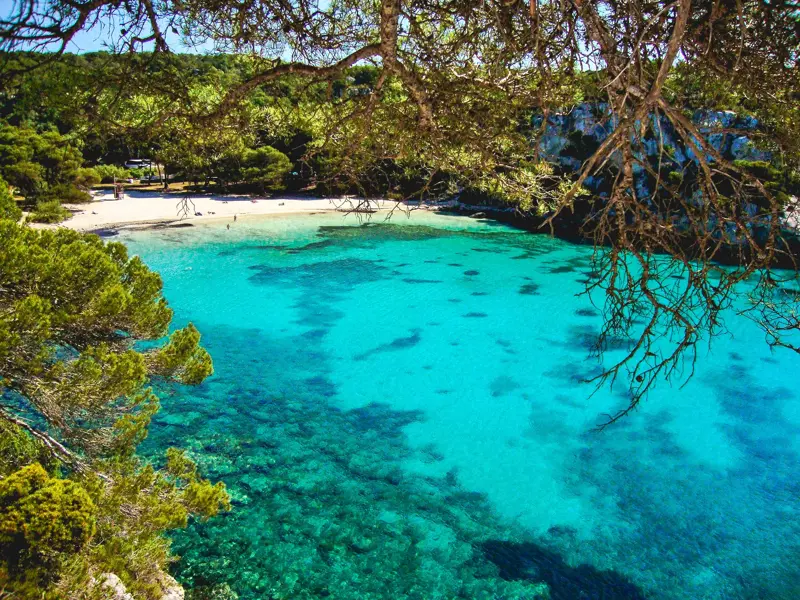 Erhöhter Blick vom Küstenwanderweg auf die Bucht Cala Macarella auf Menorca mit türkisfarbenem Meer und Sandstrand.