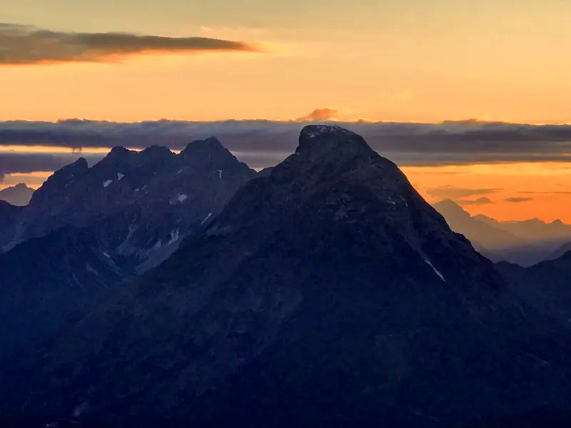 Die schroffen Gipfel des Karwendelgebirges als dunkle Silhouette vor einem farbenprächtigen Sonnenuntergangshimmel.