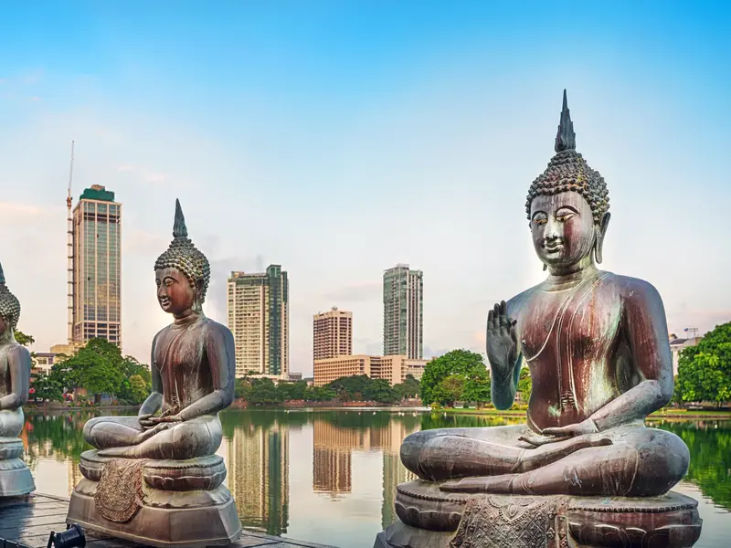 Drei sitzende Buddha-Statuen am Seema Malaka Tempel am Beira See vor der modernen Skyline von Colombo bei Tageslicht.