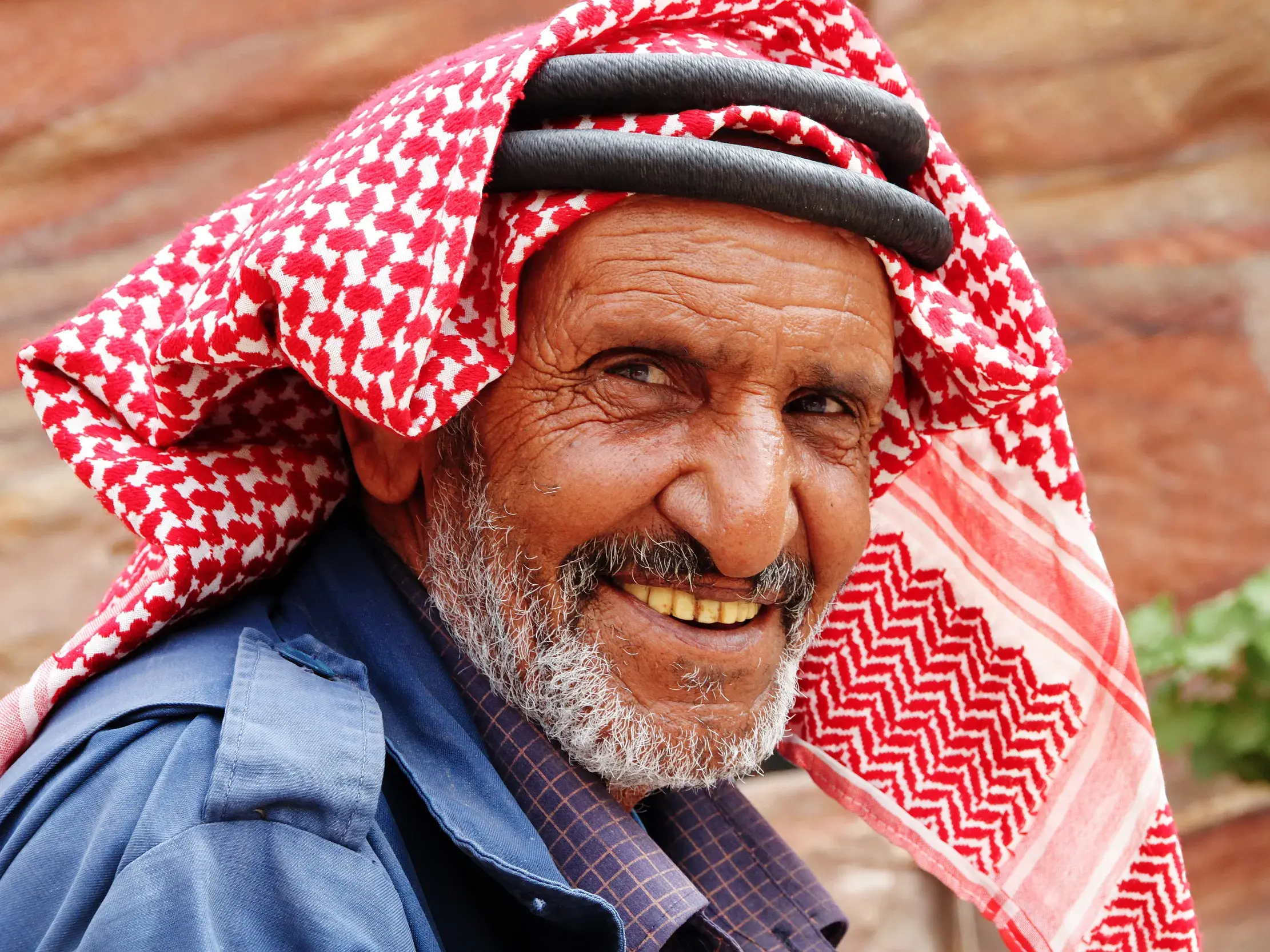 Ein älterer, lächelnder Beduine mit traditioneller Kufiya in Jordanien, eine authentische Begegnung auf der Reise.