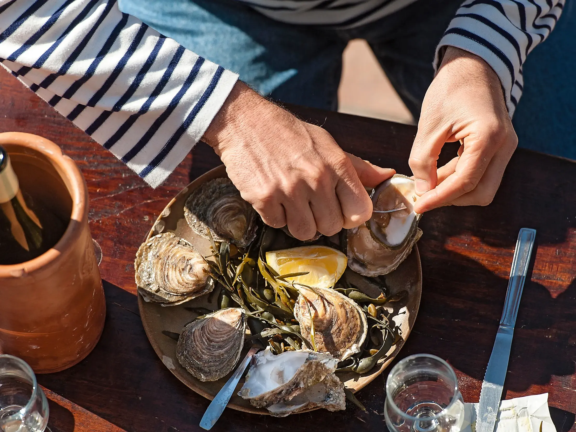Ein Mann im bretonischen Ringelshirt öffnet fachmännisch eine frische Auster bei einer Verkostung in Cancale.