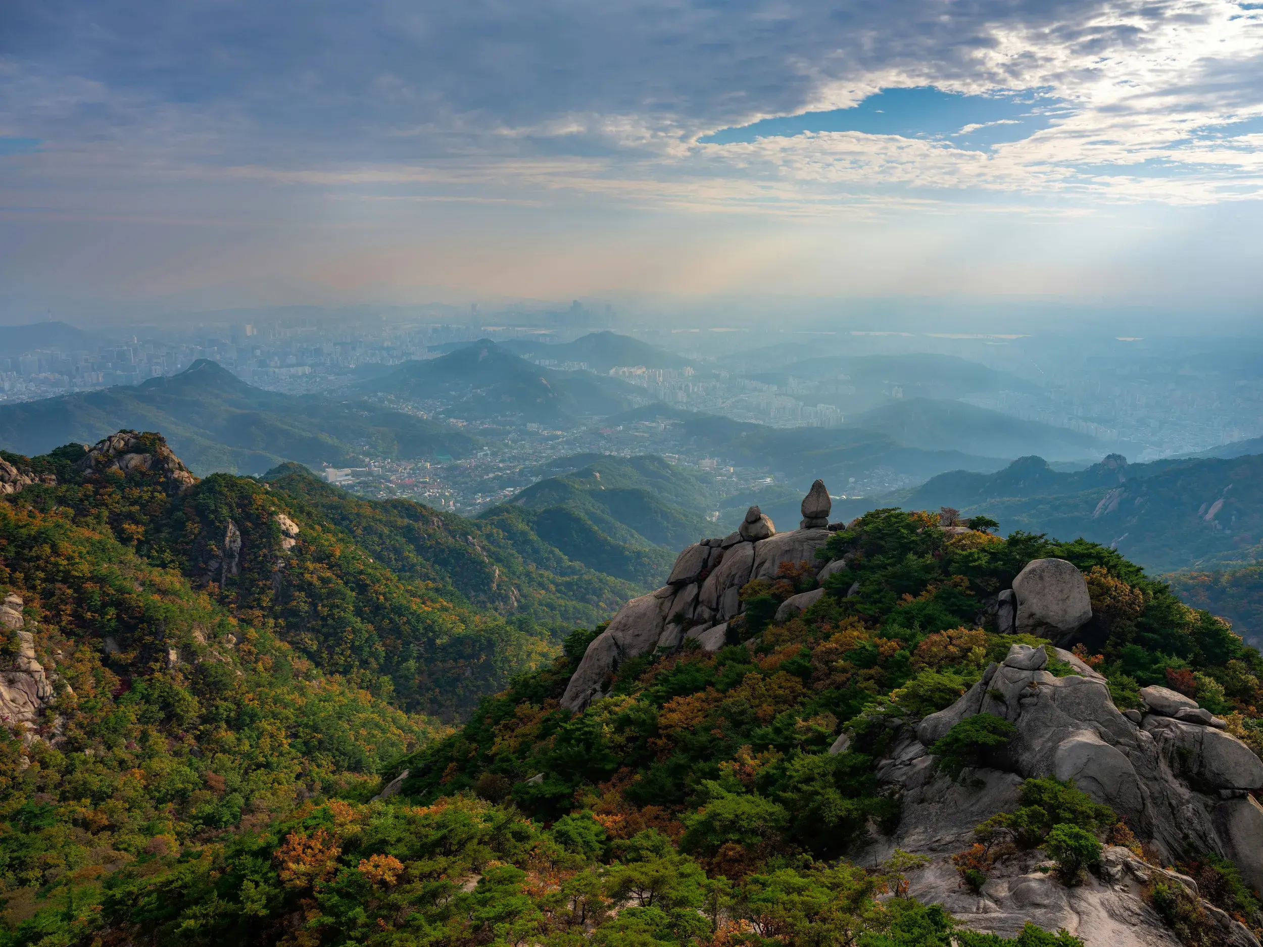 Panoramablick von den Granitfelsen des Bukhansan-Nationalparks auf die im Dunst liegende Metropole Seoul in Südkorea.