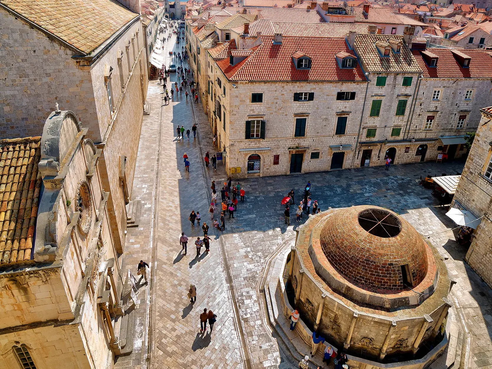 Blick von der Stadtmauer auf die belebte Hauptstraße der Altstadt von Dubrovnik, vorbei am Franziskanerkloster bei Sonnenschein.