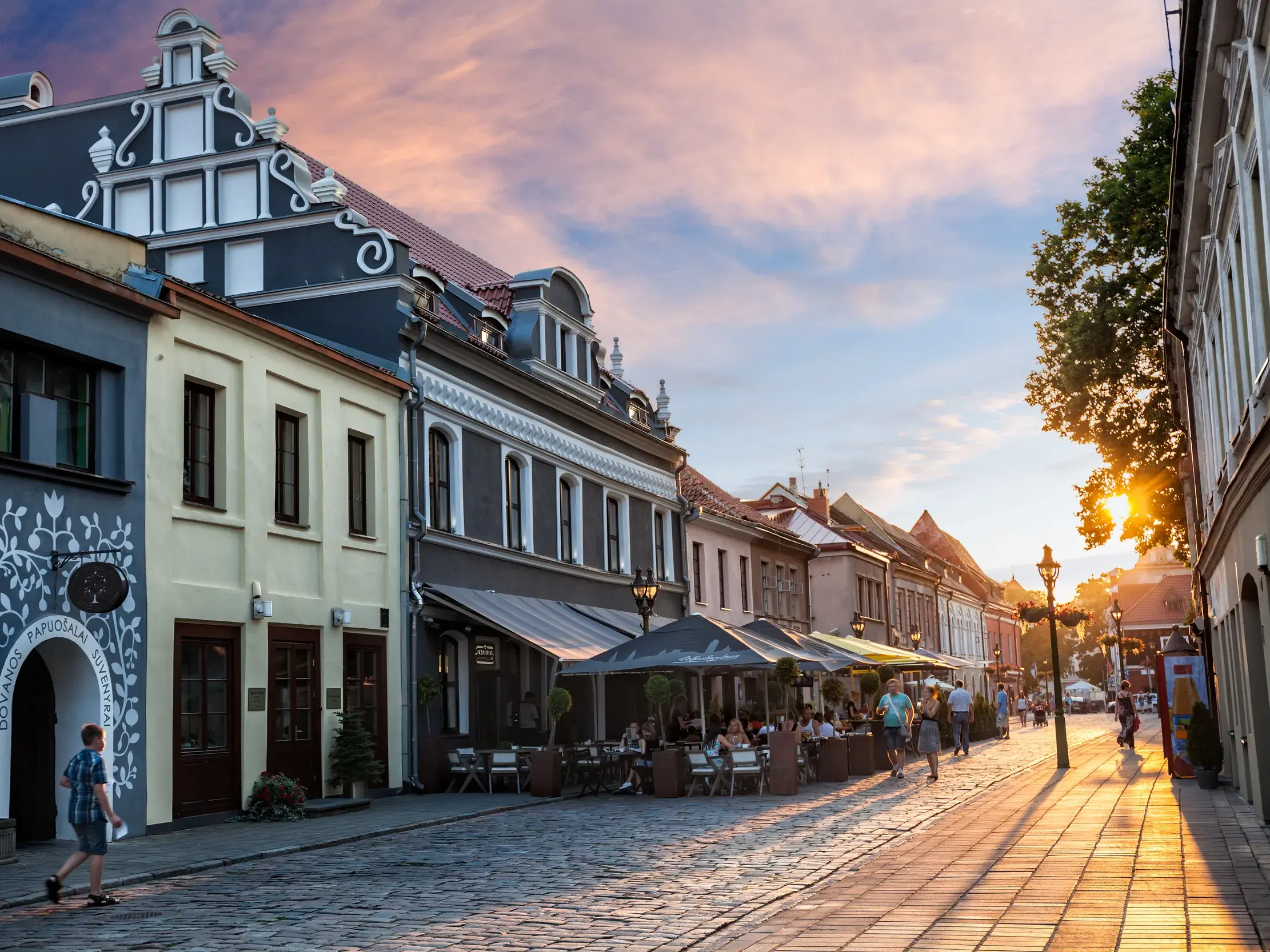 Goldene Abendsonne scheint auf eine Gasse mit Kopfsteinpflaster, bunten historischen Häusern und Cafés in der Altstadt von Klaipeda.