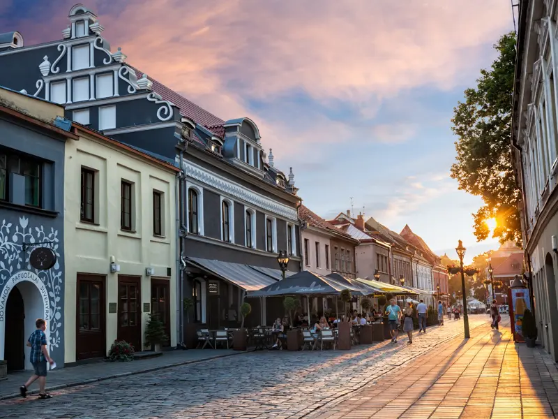 Goldene Abendsonne scheint auf eine Gasse mit Kopfsteinpflaster, bunten historischen Häusern und Cafés in der Altstadt von Klaipeda.