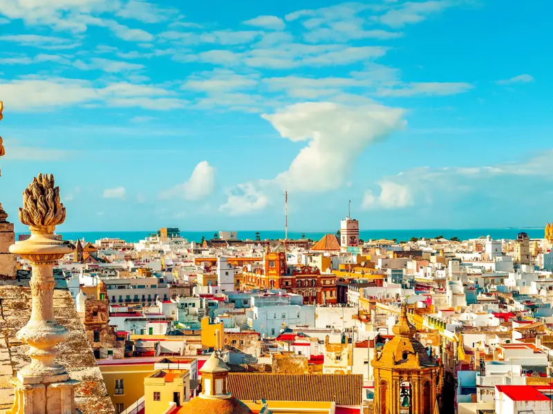 Sonniger Panoramablick von einer Kathedrale über die weißen Häuser der Altstadt von Cádiz bis zum blauen Atlantik.