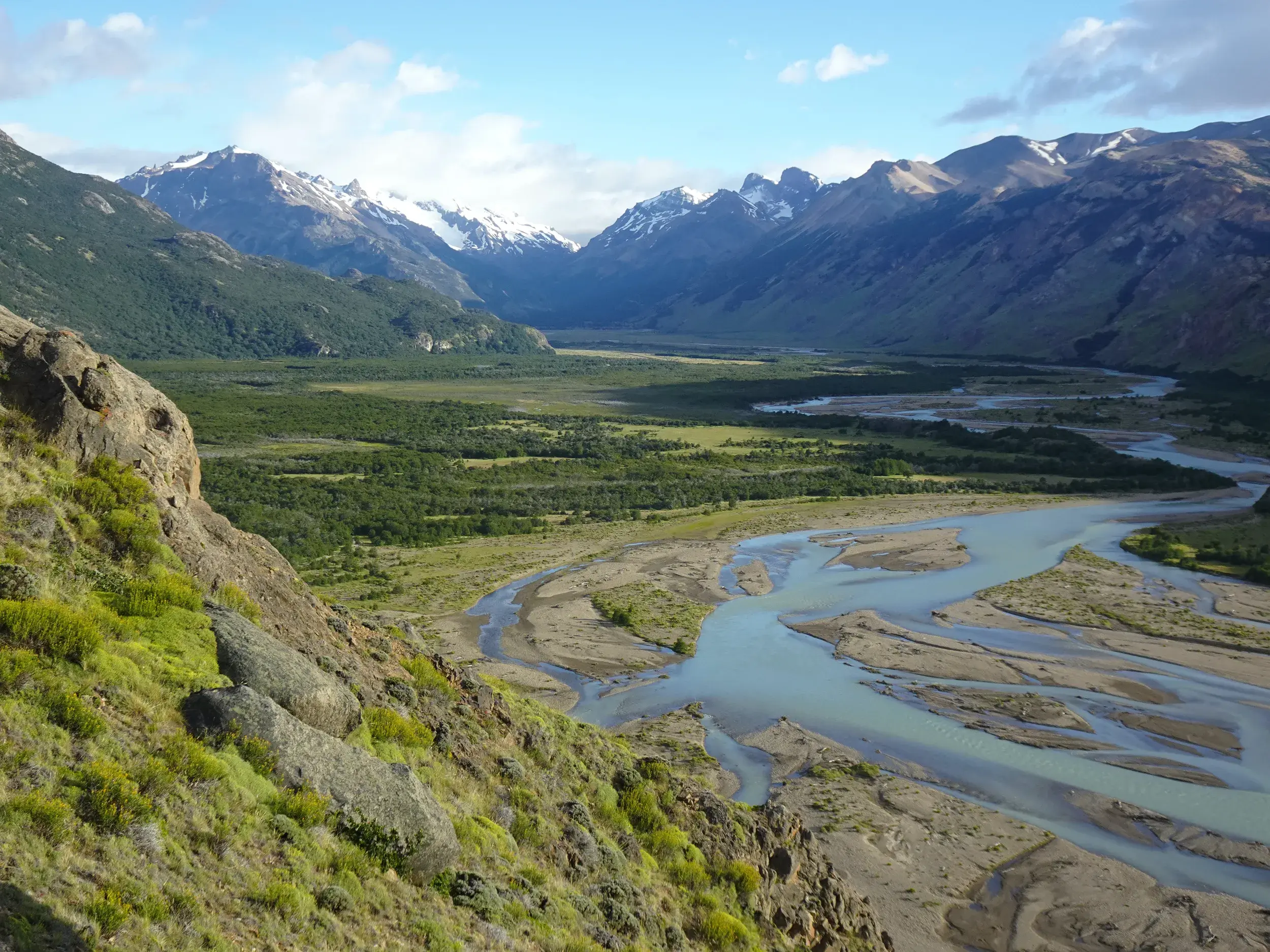 Aussicht beim Trekking nahe El Chaltén auf ein weites Flusstal und die majestätischen, schneebedeckten Anden Patagoniens.