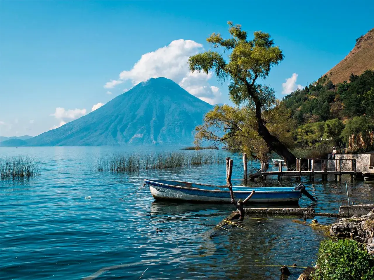 Ein kleines Boot liegt am Ufer des Atitlán-Sees in Guatemala, im Hintergrund ragt der Vulkan San Pedro in den Himmel.