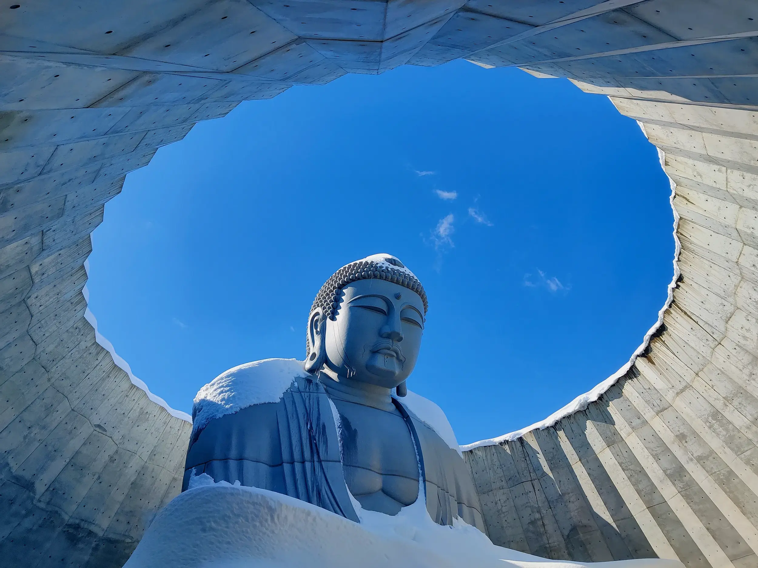 Die schneebedeckte Riesenbuddha-Statue von Tadao Ando in Hokkaido in einer Betonkuppel unter strahlend blauem Winterhimmel.
