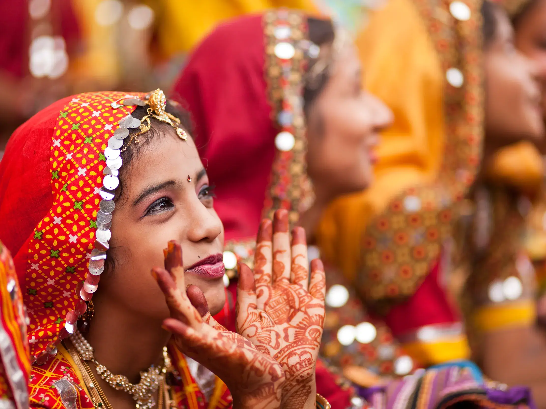Junge indische Frau mit Henna-bemalten Händen in traditioneller Kleidung bei einer farbenfrohen Zeremonie in Indien.