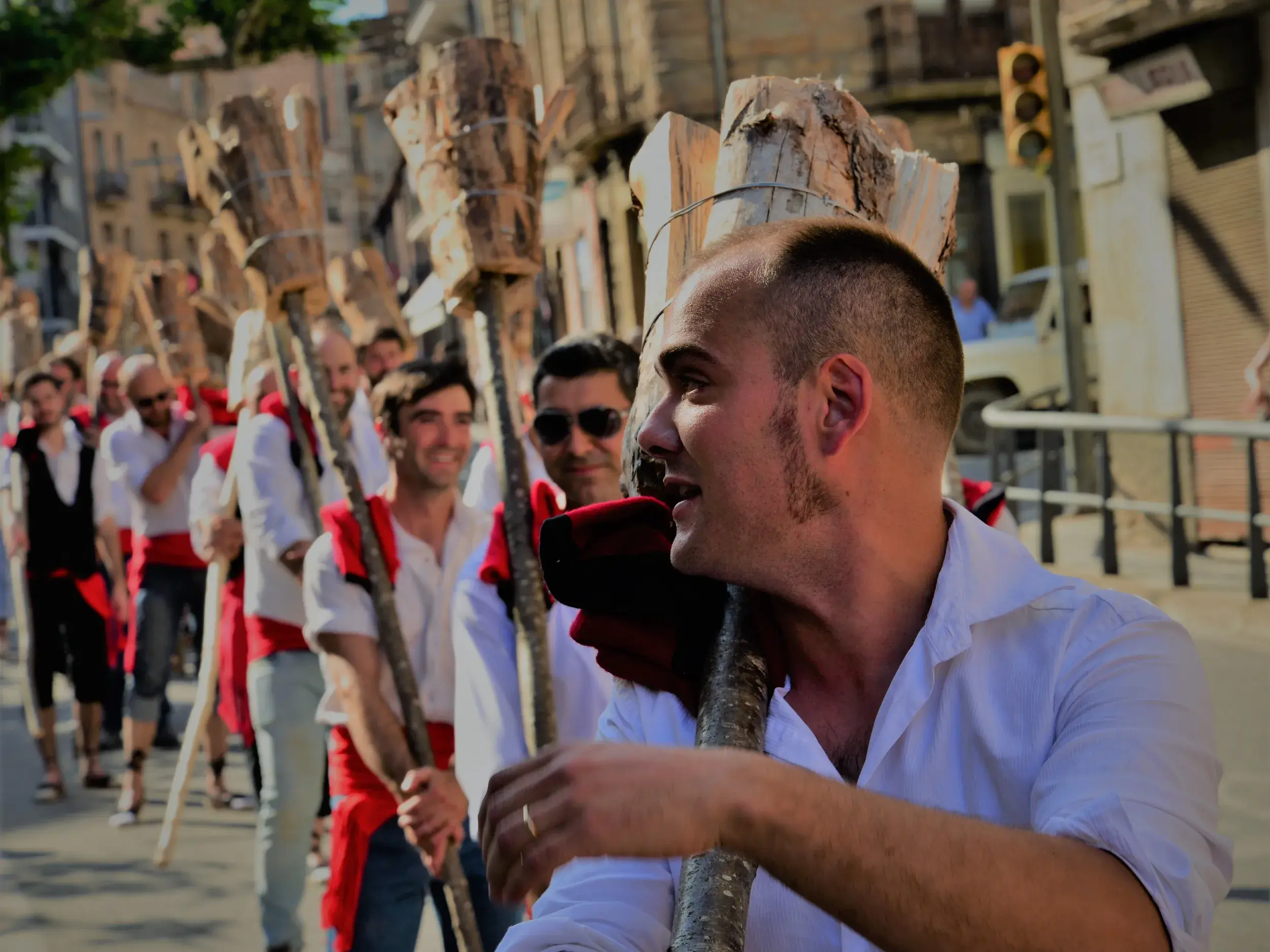 Einheimische Männer in weißen Hemden tragen bei einem traditionellen Festumzug in den Pyrenäen massive Holzstämme auf den Schultern.