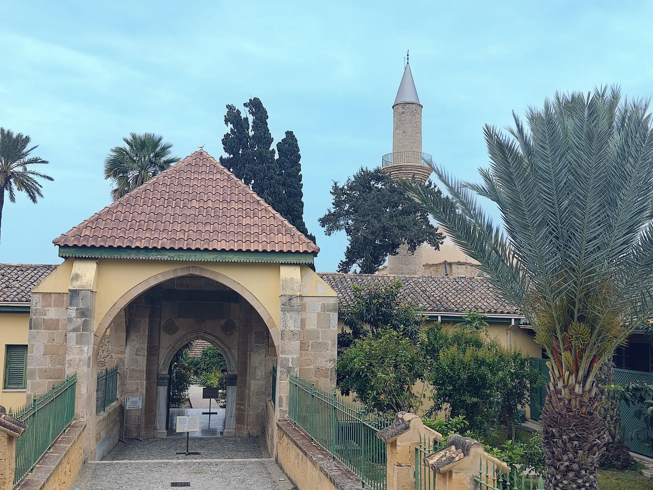 Eingangstor und Minarett der Hala-Sultan-Tekke Moschee in Larnaka, umgeben von mediterranen Palmen und Zypressen.
