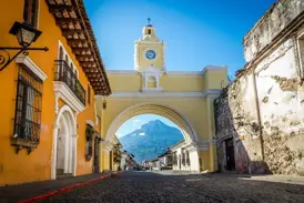 Kopfsteinpflasterstraße in Antigua mit dem gelben Arco de Santa Catalina, der den Vulkan Agua an einem sonnigen Tag einrahmt.