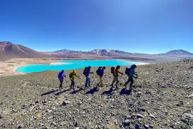 Sechs Bergsteiger einer Trekking-Gruppe wandern mit Stöcken an der türkisfarbenen Laguna Verde in der Atacama-Wüste in Chile.