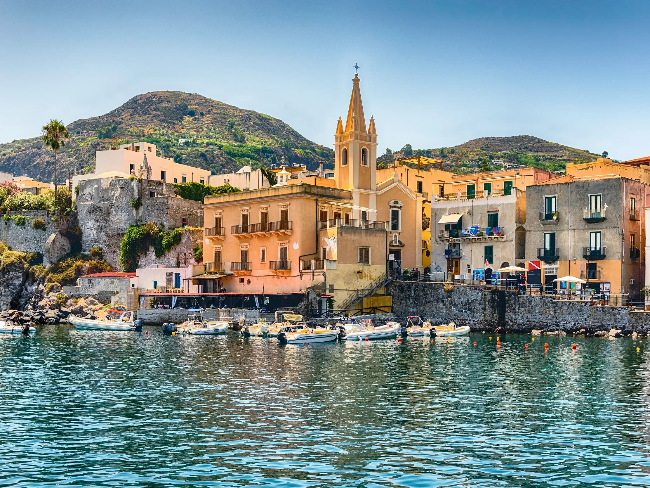 Malerische Hafenansicht von Lipari auf den Äolischen Inseln mit bunten Häusern, Kirche und kleinen Fischerbooten im Wasser.