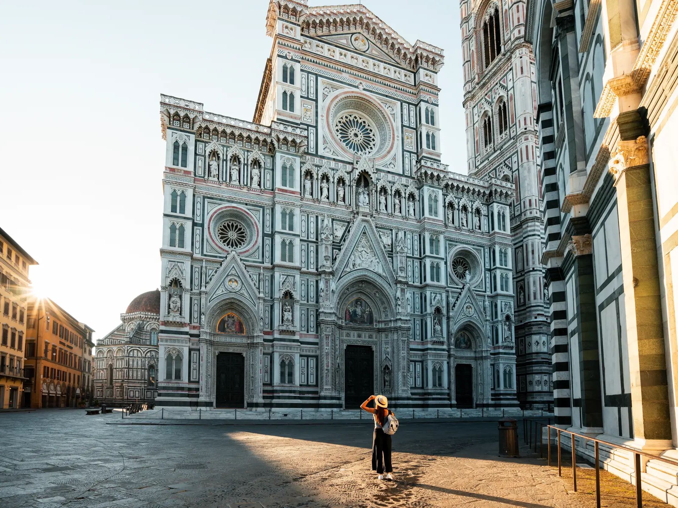 Eine Frau mit Hut blickt im frühen Morgenlicht auf die prächtige Marmorfassade des Doms von Florenz auf der Piazza del Duomo.