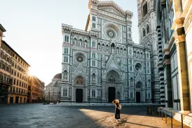 Eine Frau mit Hut blickt im frühen Morgenlicht auf die prächtige Marmorfassade des Doms von Florenz auf der Piazza del Duomo.