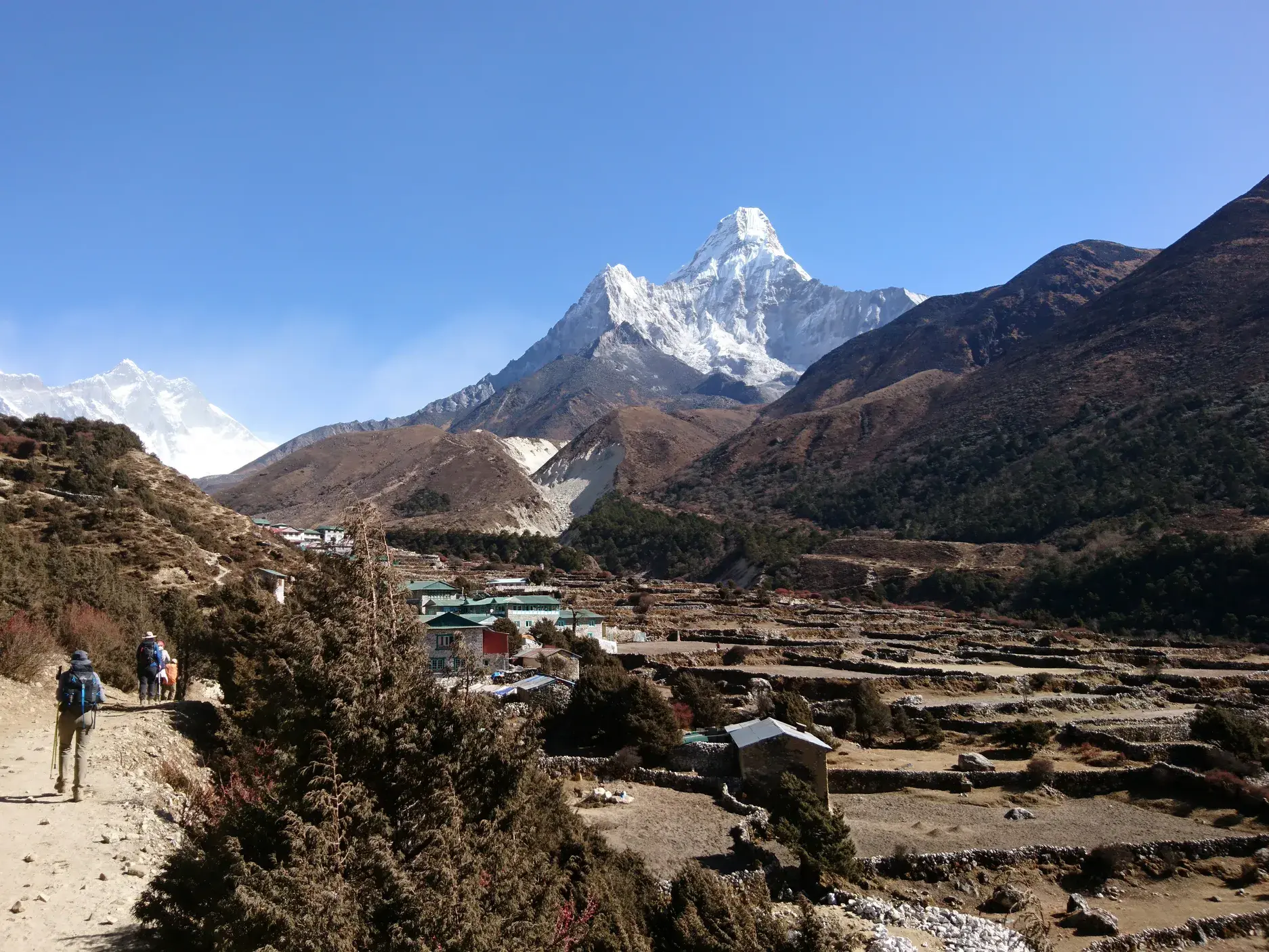 Eine Wandergruppe auf einem Pfad im Khumbu-Tal in Nepal mit Blick auf den schneebedeckten Gipfel der Ama Dablam.